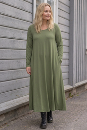 Blond modell i grön Ballerina Long Sleeve, lätt lutande mot träfasaden